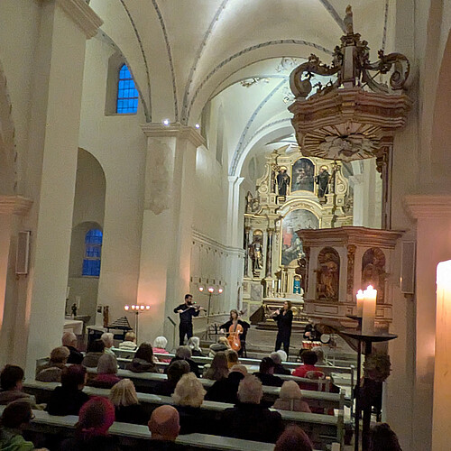 Blick in Kirchinnenraum mit vollbesetzten Bänken, vorne spielen vier Musiker.
