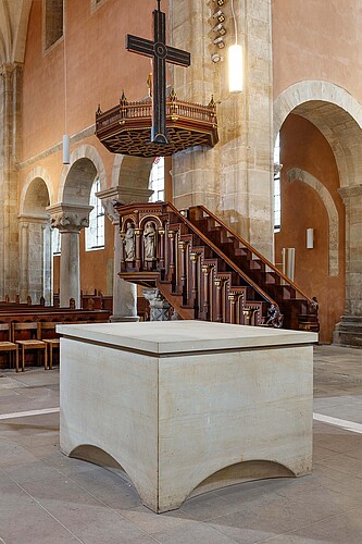 Blick auf einen modernen Altar mit einem Kreuz, das darüber aufgehängt ist, und die Kanzel nach der Instandsetzung.