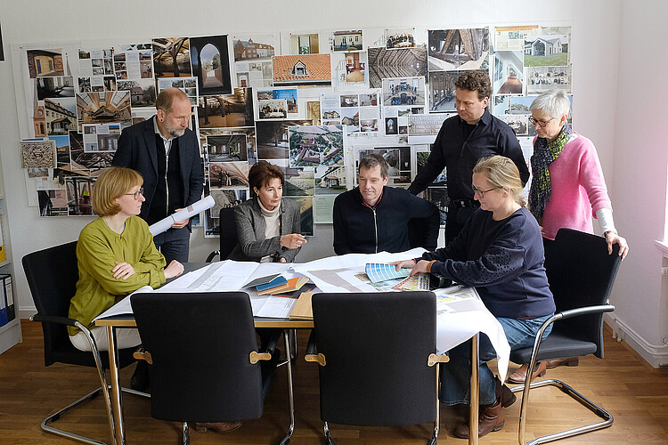 Vier Männer und drei Frauen, darunter Rita Hoheisel, Leiterin der Abteilung für Bau- und Kunstpflege der Klosterkammer, stehen um einen Tisch auf dem Pläne und Proben für Baumaterial liegen.
