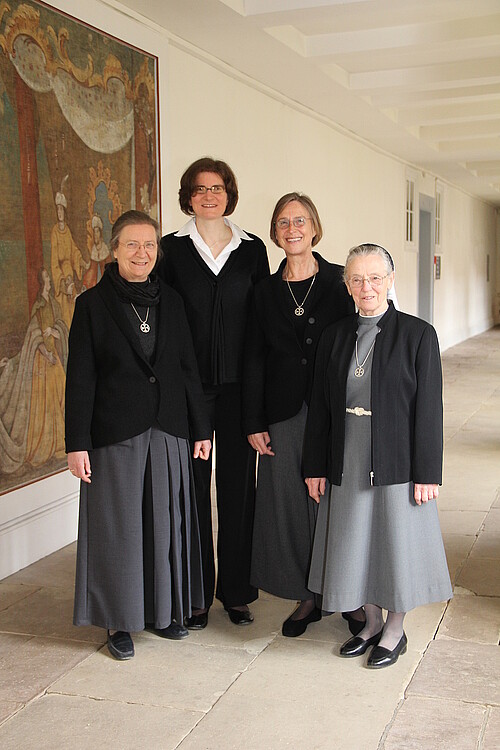Vier Frauen in dunkler Kleidung stehen in einem Kreuzgang.