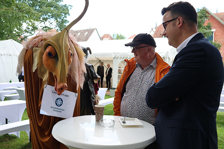 Ein Mensch als Einhorn verkleidet steht an einem Tisch mit Gästen des Klosterkammertages.