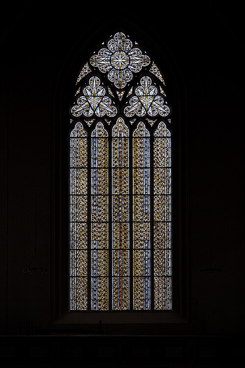 Ein düster umrandetes Kirchenfenster mit gotischem Bogen.