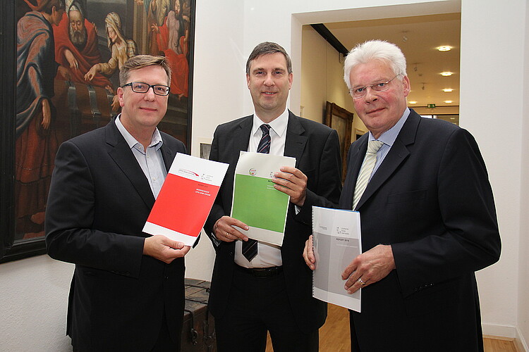 Drei Herren halten jeweils Broschüren in der Hand - sie präsentierten Ergebnisse der Studie "Learning from Partners":