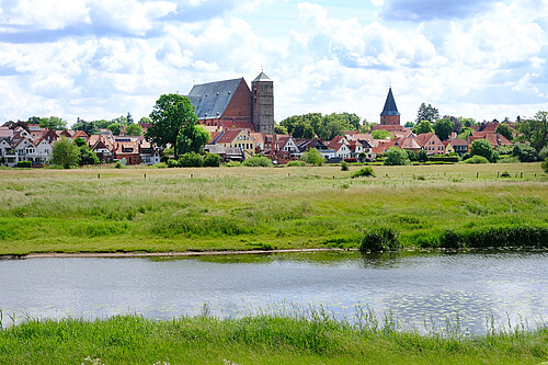 Im Vordergrund sind der Fluss Aller und wiesen zu sehen, dahinter die Silouette der Stadt Verden.