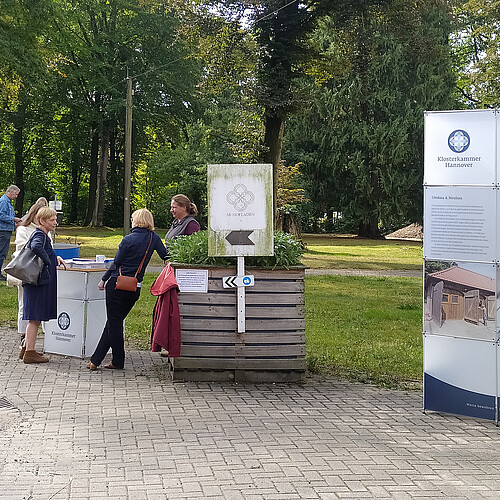 Gutspark Burgsittensen, Menschen stehen an einem Stehtisch, daneben befindet sich eine Infowand.