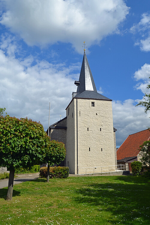 Frontansicht eines hell gestrichenen, rechteckigen Kirchturmes mit spitzem Dach.