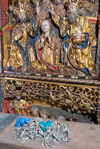 Drei Figuren des Altarreliefs in Nahaufnahme - davor liegen Schwämmchen, die zur Reinigung verwendet wurden.