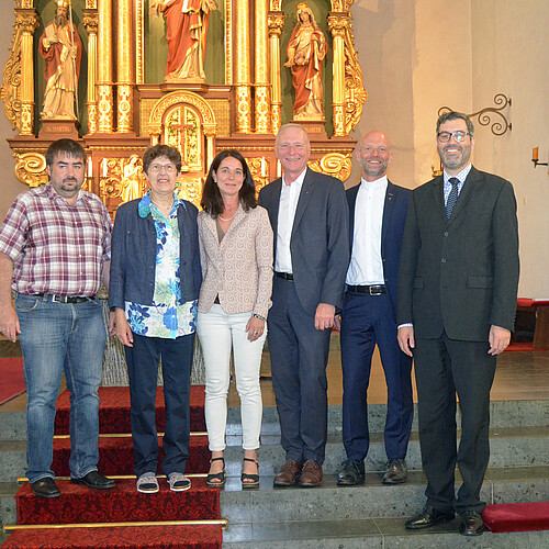 Zwei Frauen und vier Männer stehen im Innenraum einer Kirche auf einer Treppe.
