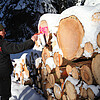 Ein Stapel Stämme ist mit Schnee bedeckt, davor steht ein Mann der sie mit farbigen Markierungen besprüht.