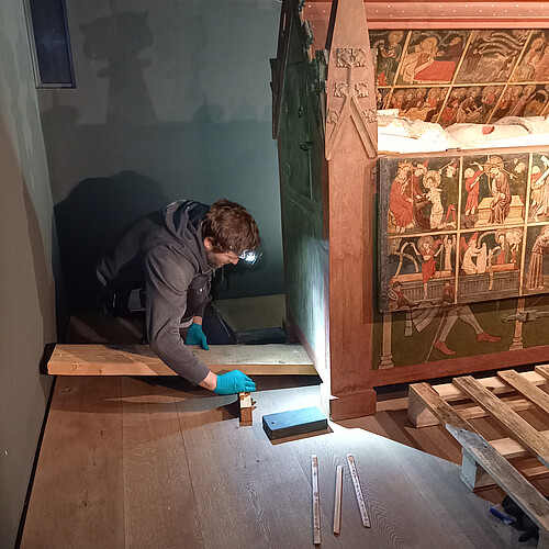 Restaurator Johannes Mädebach kniet neben einen großen Kunstwerk aus Holz, um dieses aufbocken und so vor hereinlaufendem Wasser schützen zu können.