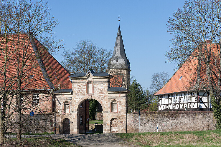 Ein Torbogen aus hellem Stein, der restauriert worden ist. Im Hintergrund ist ein Kirchturm zu sehen.