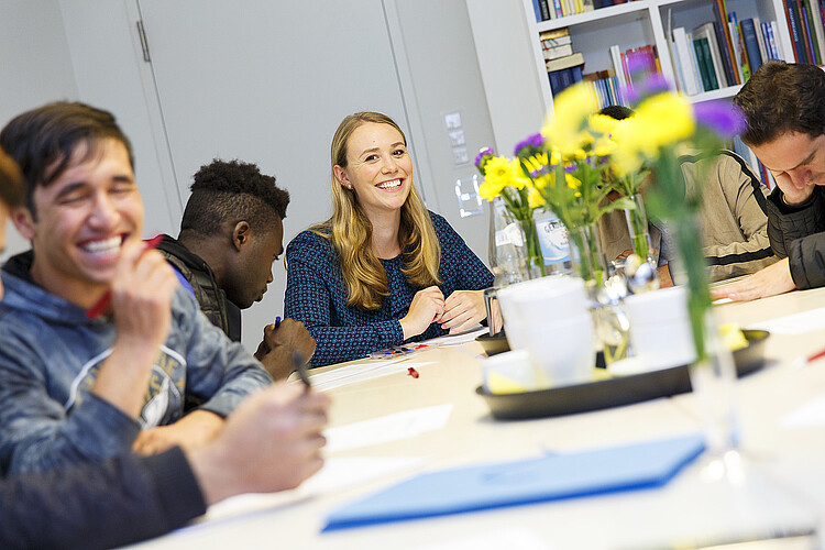 Anna Bertram unterstützt Flüchtlinge beim Deutschunterricht im Eine junge Frau sitzt gemeinsam mit geflüchteten Jugendlichen an einem Tisch.